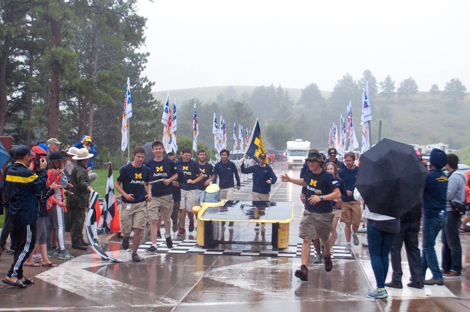 Members of the Michigan Solar Car team run across a finish line alongside their car, Aurum, in the rain.
