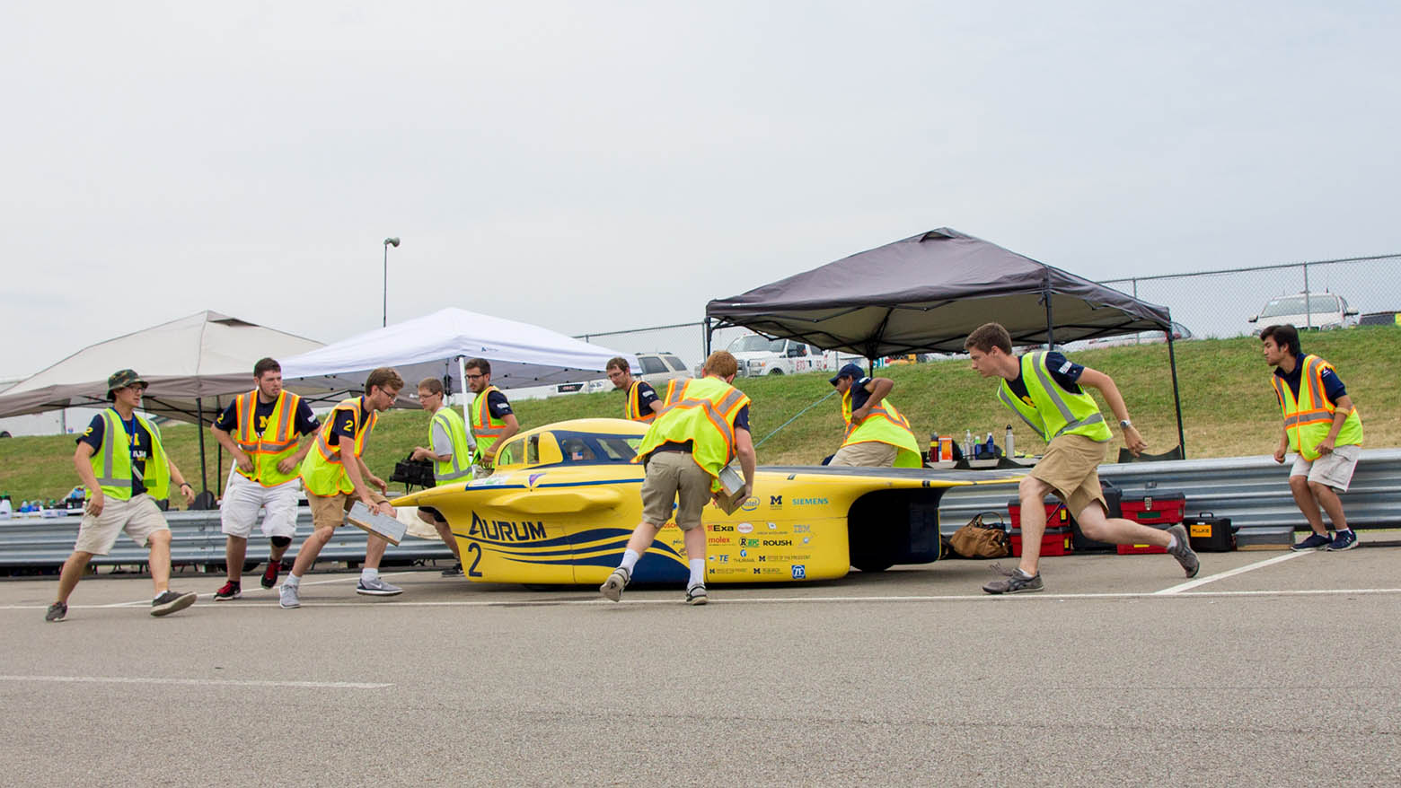 Members of the Michigan Solar Car team race to surround their car, Aurum, during a pit stop at the track.