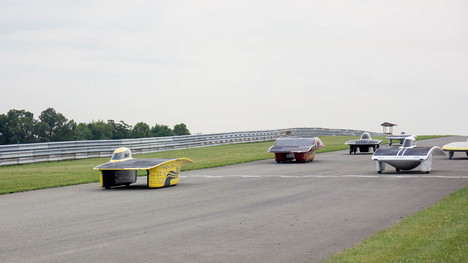 Aurum, the Michigan Solar Car, leads a pack of solar cars across the starting line at a race track.