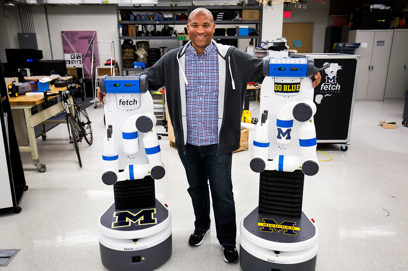 Chad Jenkins, CSE Associate Professor, poses with his research group's two robots, Odd Job and Cookie.