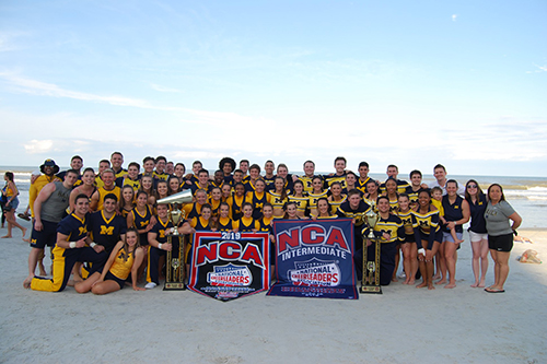 group photo of Michigan cheer squad on the beach with NCA competition banners