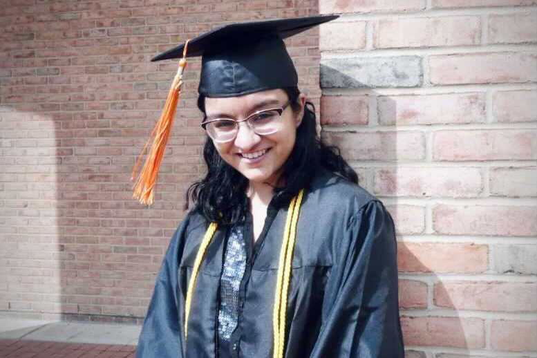 Isha Bhatt in grad cap and gown in front of brick wall