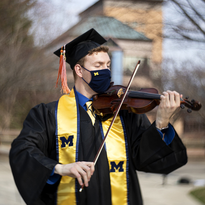 Matthew Lamb plays the violin in grad cap and gown on North Campus