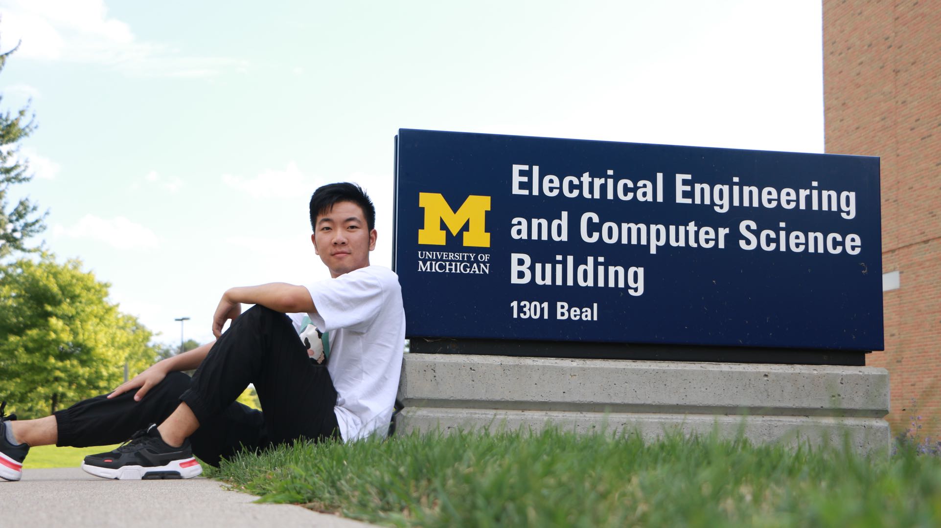 Puhua Jiang leans against the EECS building sign