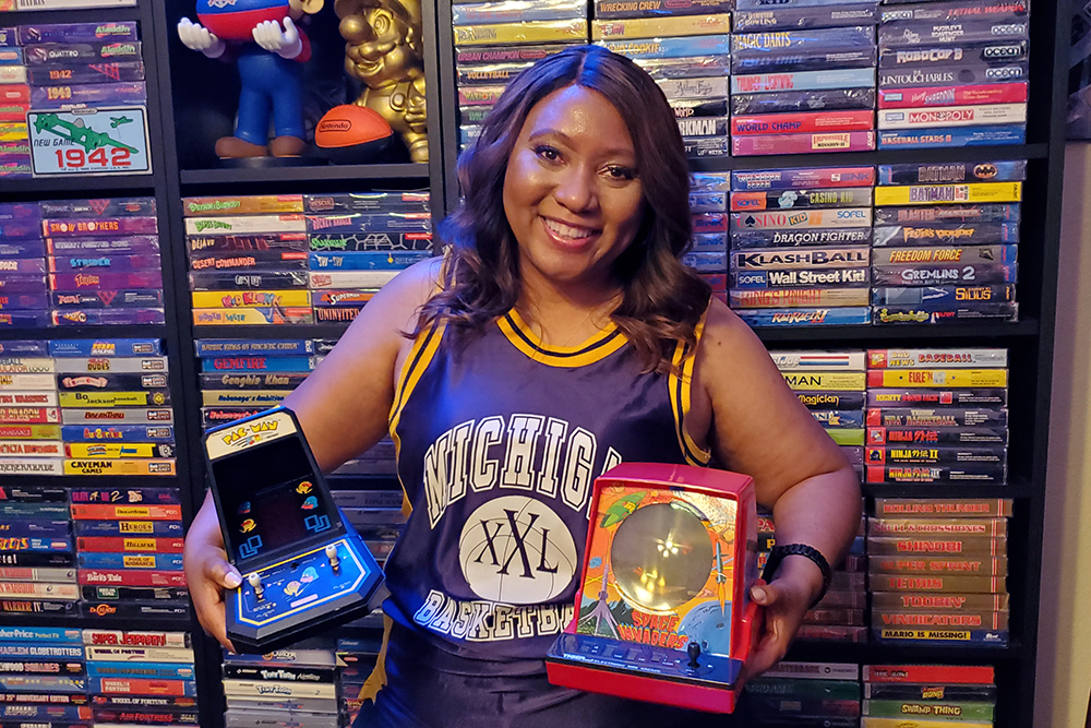 Linda Guillory holding pacman and space invaders in front of bookcase of games
