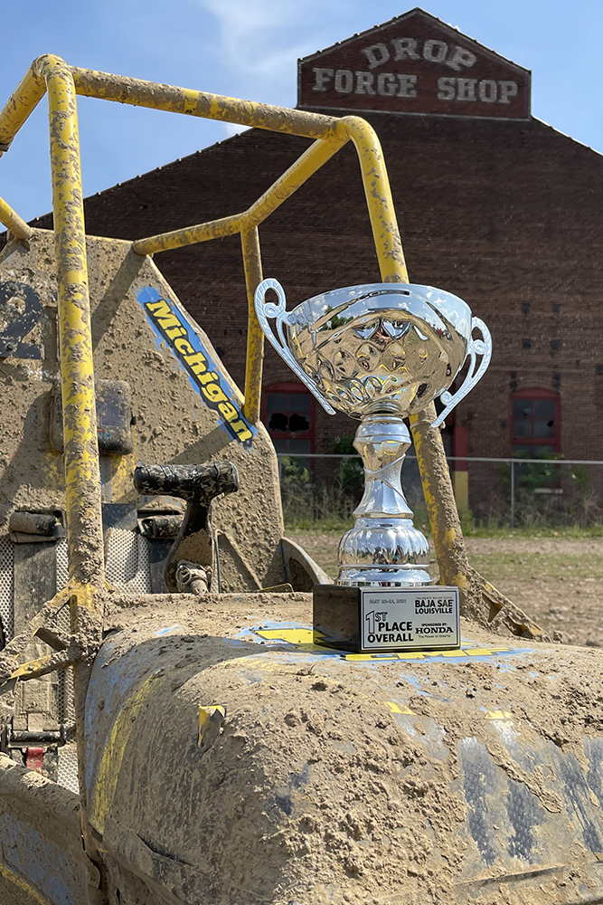 1st place trophy on top of mud-caked Michigan Baja car