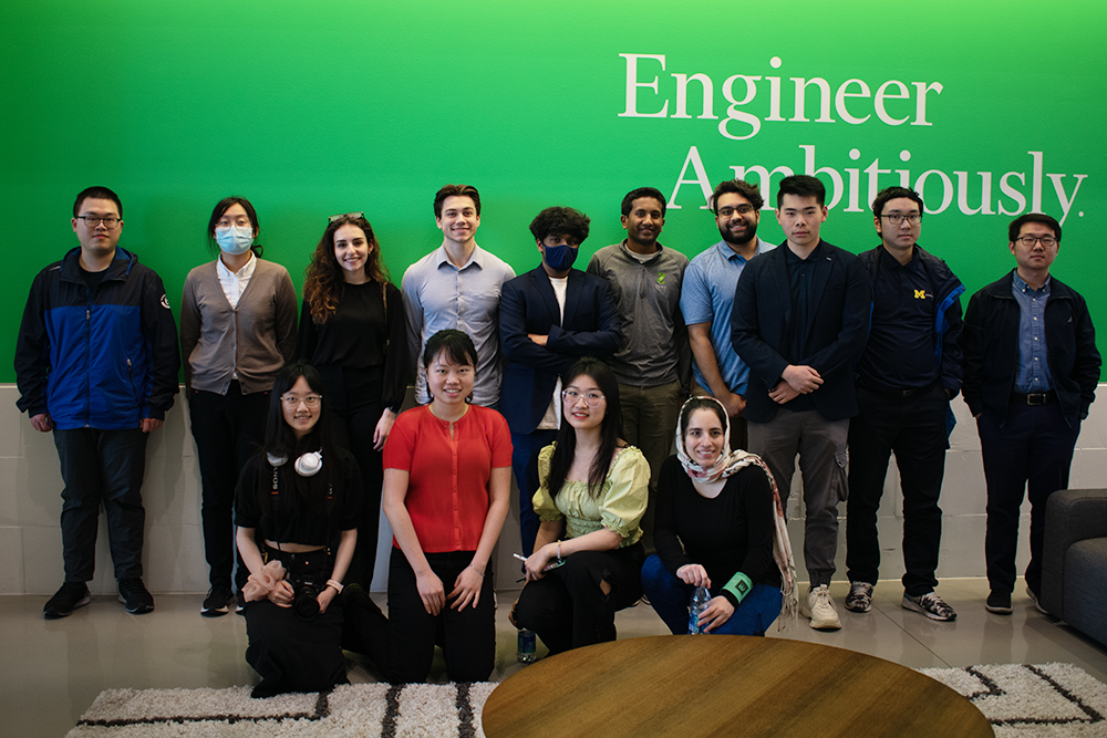 group photo in front of a green wall with white text that reads "Engineer Ambitiously"