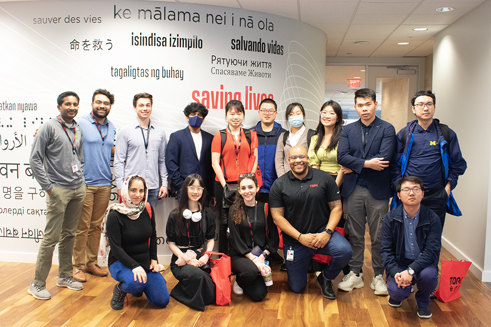 group photo in front of an office wall at Torc Robotics featuring the moto "saving lives" in many different languages