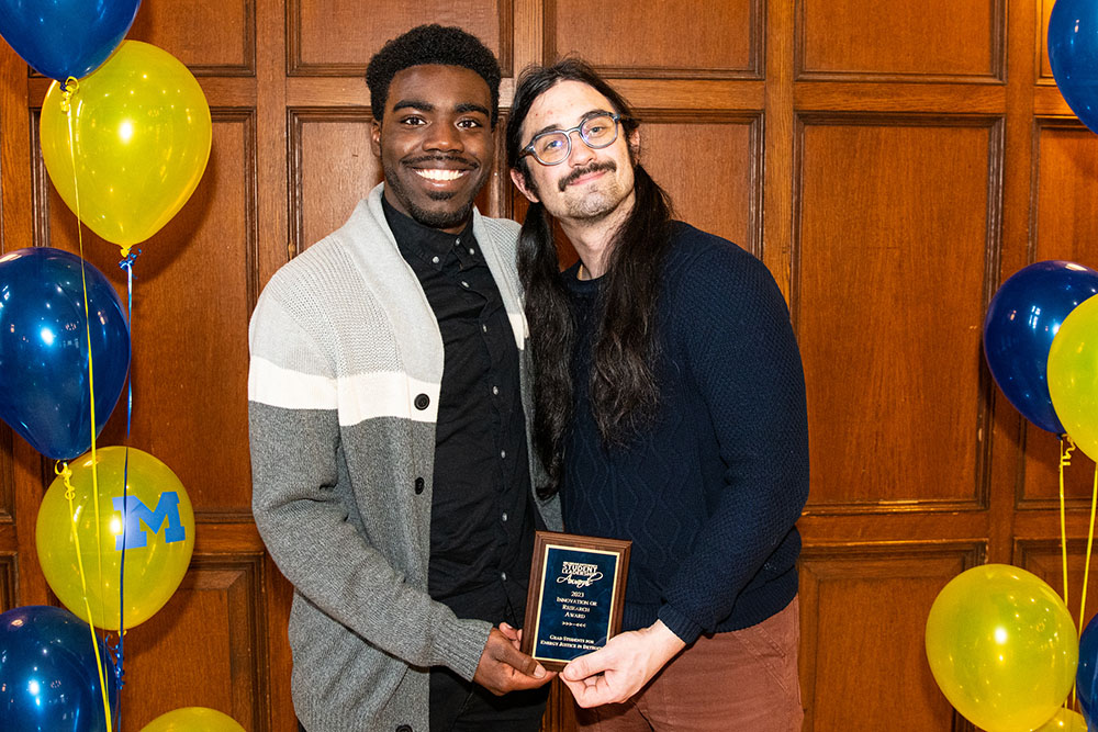 Xavier Farrell and Joshua Brooks hold the award plaque at the ceremony surrounded by U-M balloons