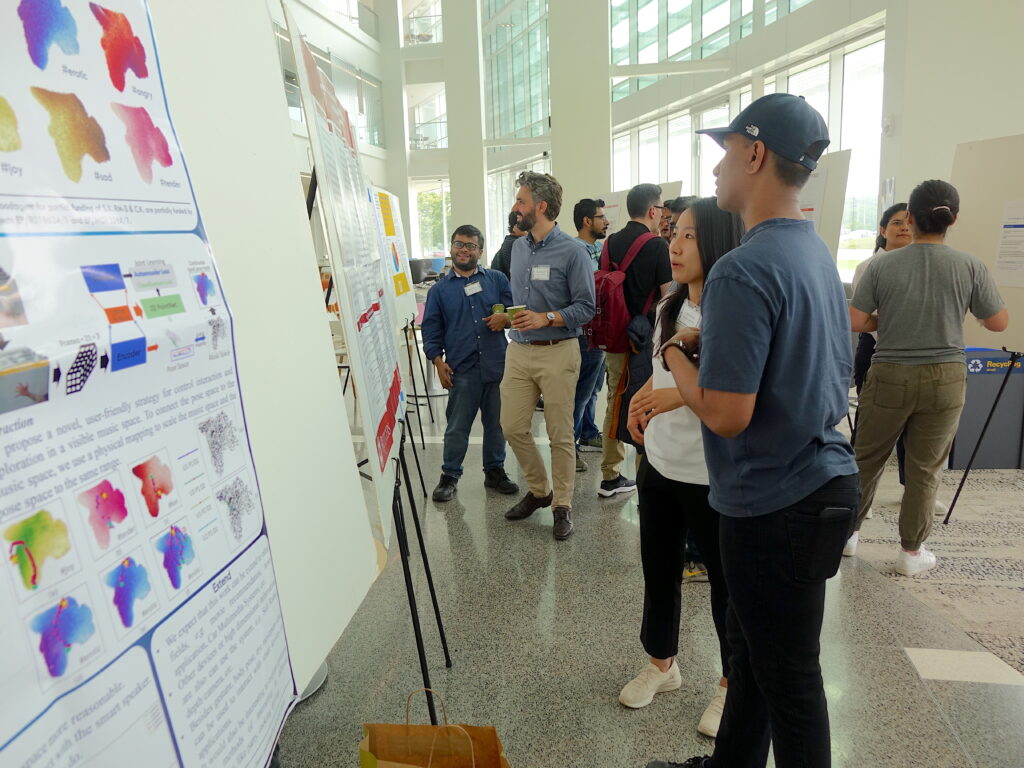 A group of students and faculty stand in front of posters on stands discussing their research