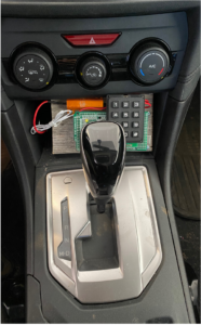 Car shifter and dashboard with prototype keypad installed underneath A/C controls. The devices consists of a numeric keyboard, circuit, and wires.