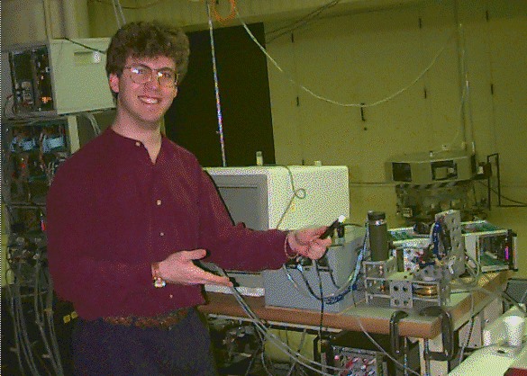 Charles Cohen gesturing to a robot set up on a table in a dark, windowless lab