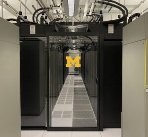 Photo of the Michigan Academic Computing Center (MACC) with a long hallway with data servers on either side enclosed with a glass door with a block M on it.