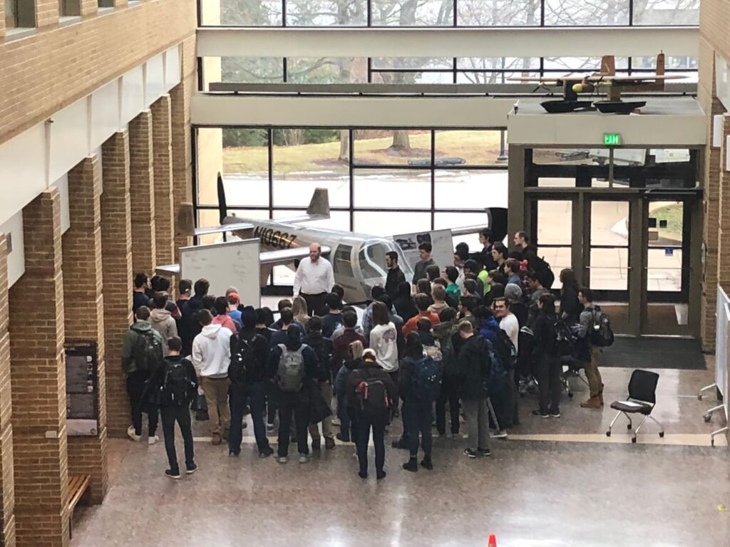 group of students stand in front of a Nomad aircraft in the François-Xavier Bagnoud Building.