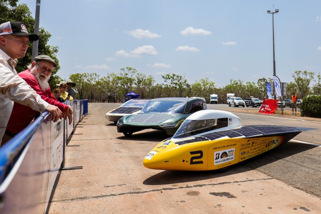 the solar car parked next to two other solar cars with bystanders standing near them 
