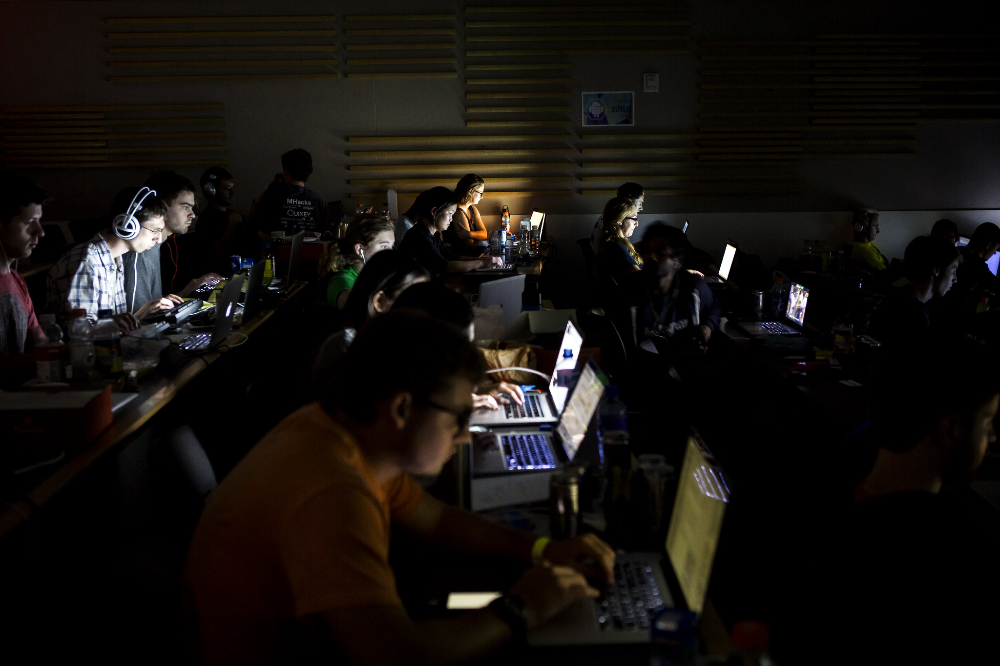 Rows of students in a lecture hall in the dark, their faces lit by their computer screens.