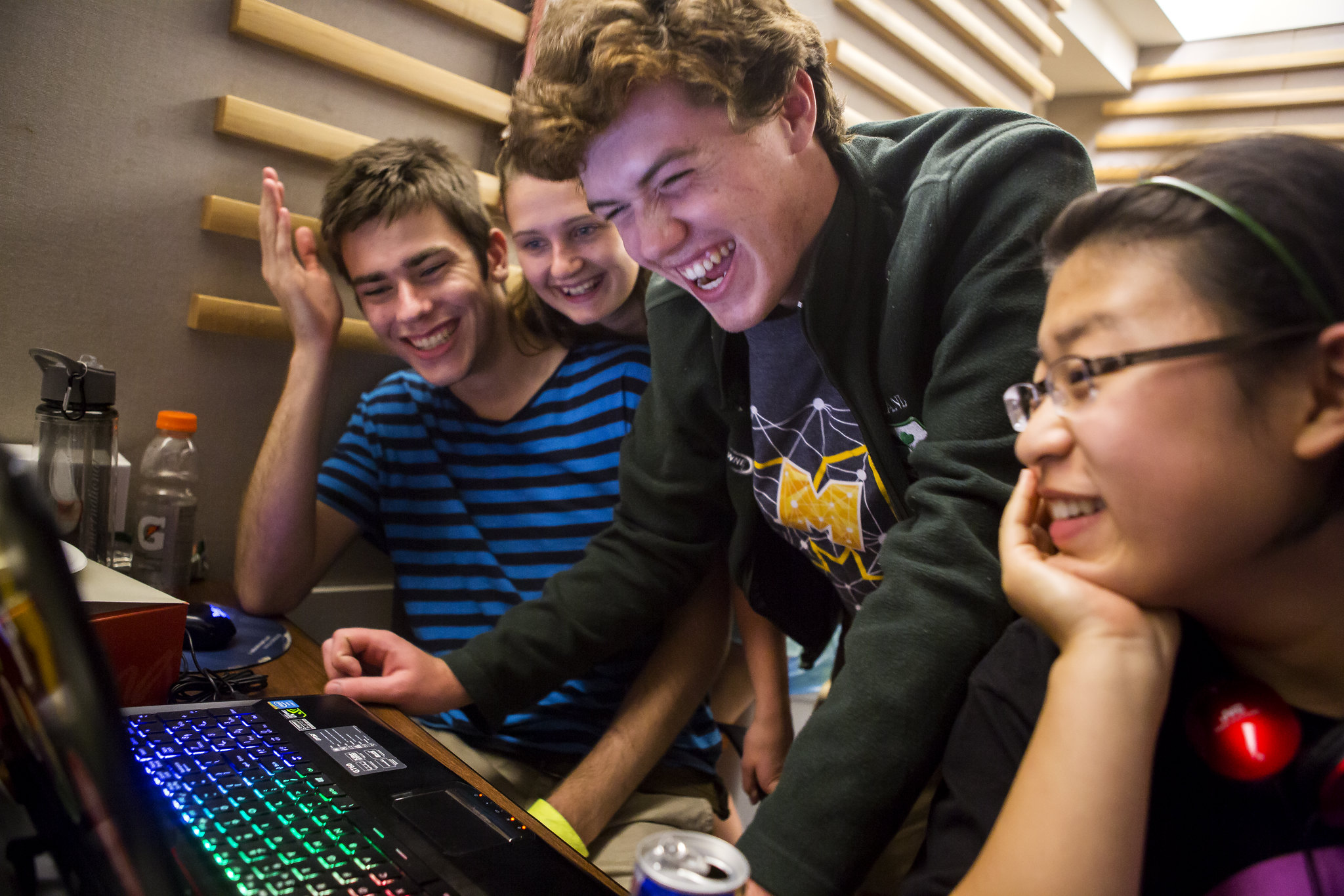Four students crowded around a computer smiling, laughing, and generally celebrating