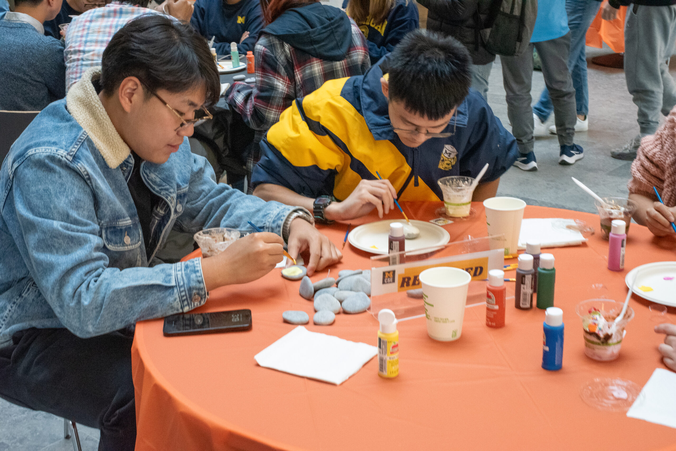 two students painting palm-sized rocks at a table with an orange table cloth