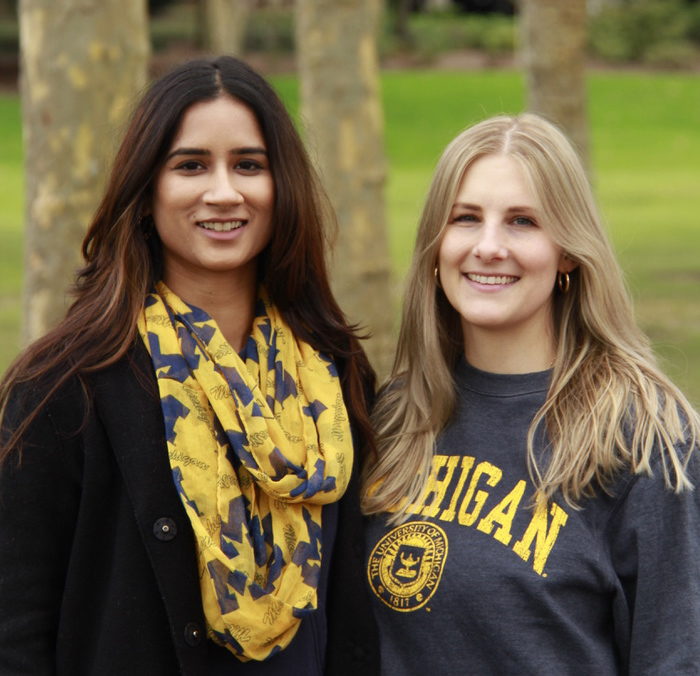 Akanksha Singh and Caitlin Short stand smiling at the camera. They are both wearing University of Michigan gear.