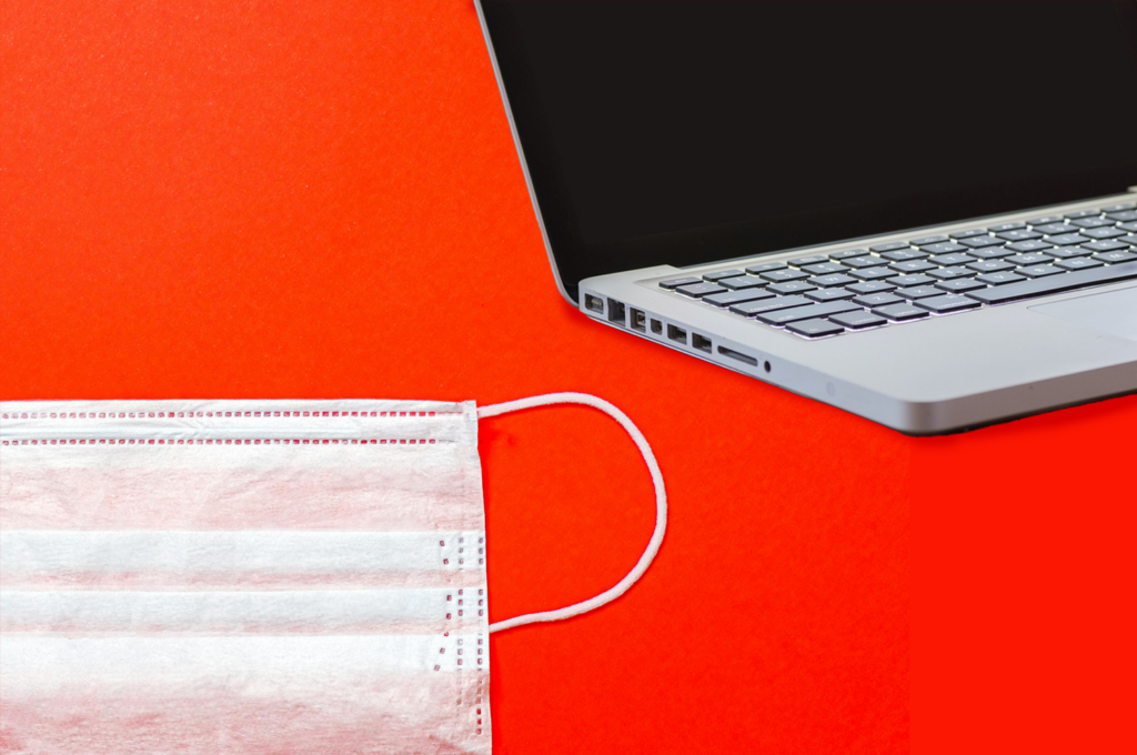A medical mask and a laptop keyboard against a bright red background