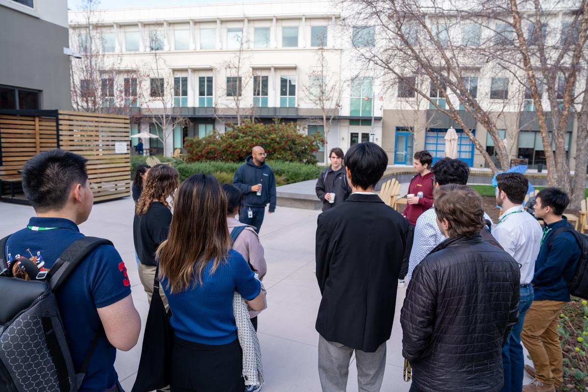 Students stand in a circle in an outdoor courtyard, listening to a tourguide.