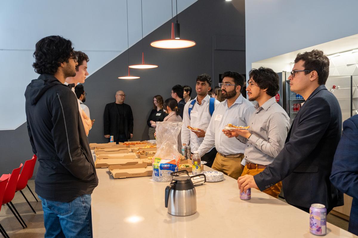 Students stand around a rectangular counter eating pizza and mingling at Kodiak Robotics.