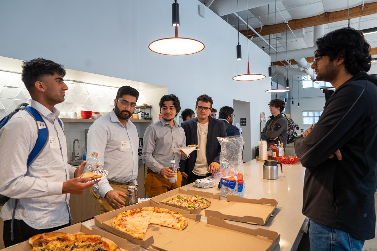 Students stand around a rectangular counter eating pizza and mingling at Kodiak Robotics.