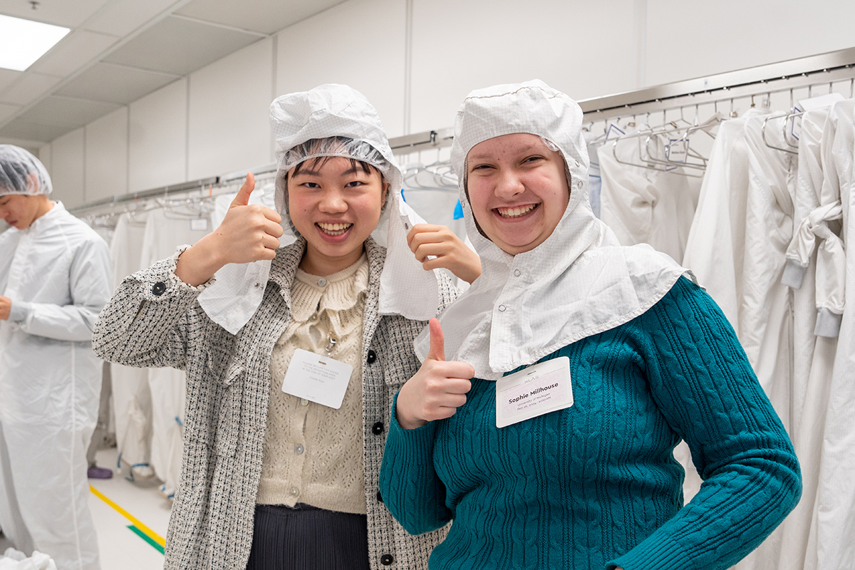 Two students pose and give thumbs up to the camera, dressed in hairnets and white hoods as part of the bunny suits.