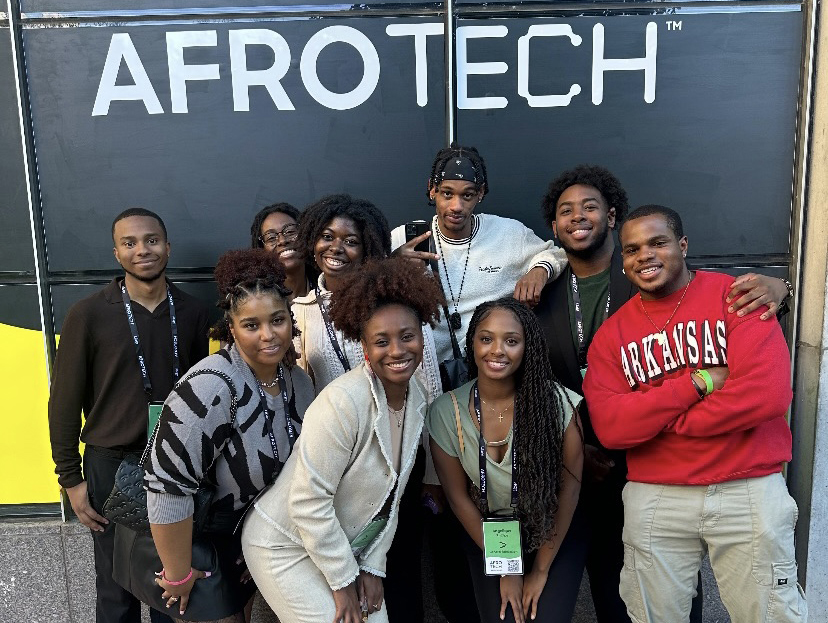 8 students stand smiling at the camera. They are standing in front of a black wall with the AfroTech logo printed in white