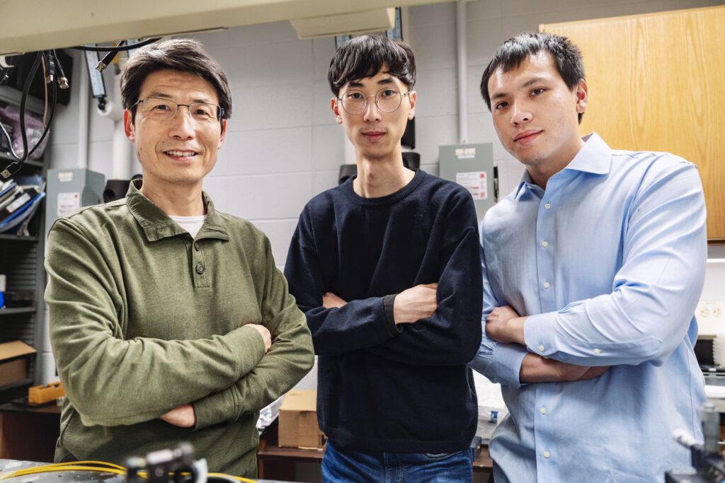 Prof. L. Jay Guo, a middle-aged man with short black hair and rectangular glasses stands, crossing his arms, in a green sweater, on the left of two members of his research group. In the middle, Hyeonwoo Kim stands with arms crossed in a black sweater. Hyeonwoo is a tall, thin person with short black hair and round glasses. On the right, Wei-Kuan Lin stands with his arms crossed in a light blue button-up shirt.