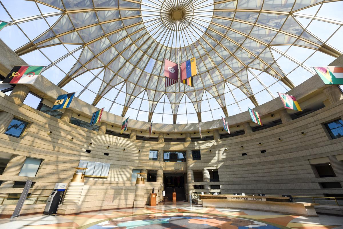 The entrance to the museum features a round, arched ceiling of geometrically-patterned glass, flags from African countries hanging around the edges of the glass ceiling, and colorful tiled artwork across the floor.