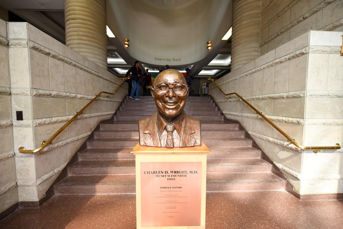A bronze bust of Dr. Charles H. Wright, a smiling Black man with glasses, depicted wearing a suit.