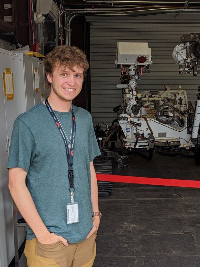 Evan Eidt standing in a garage bay in front of a piece of equipment that looks like a white robot.
