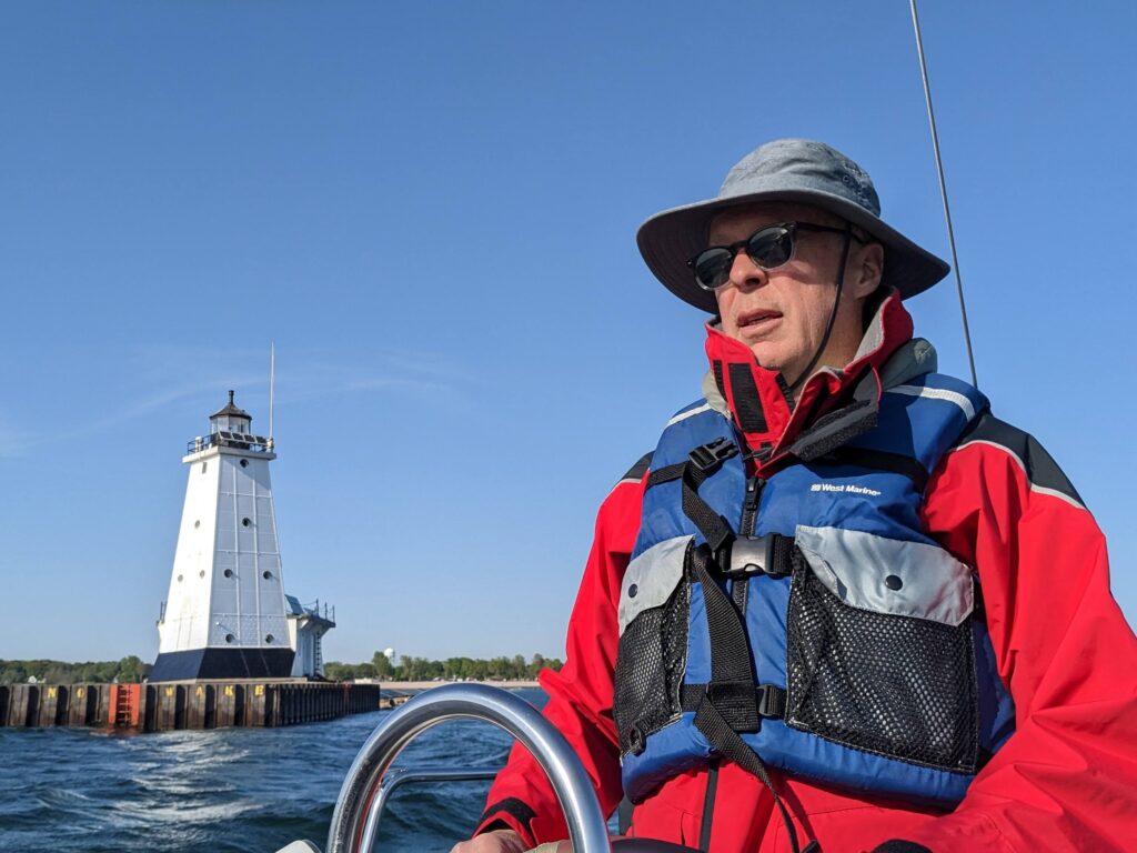 Chesney piloting his sailboat with lighthouse in background