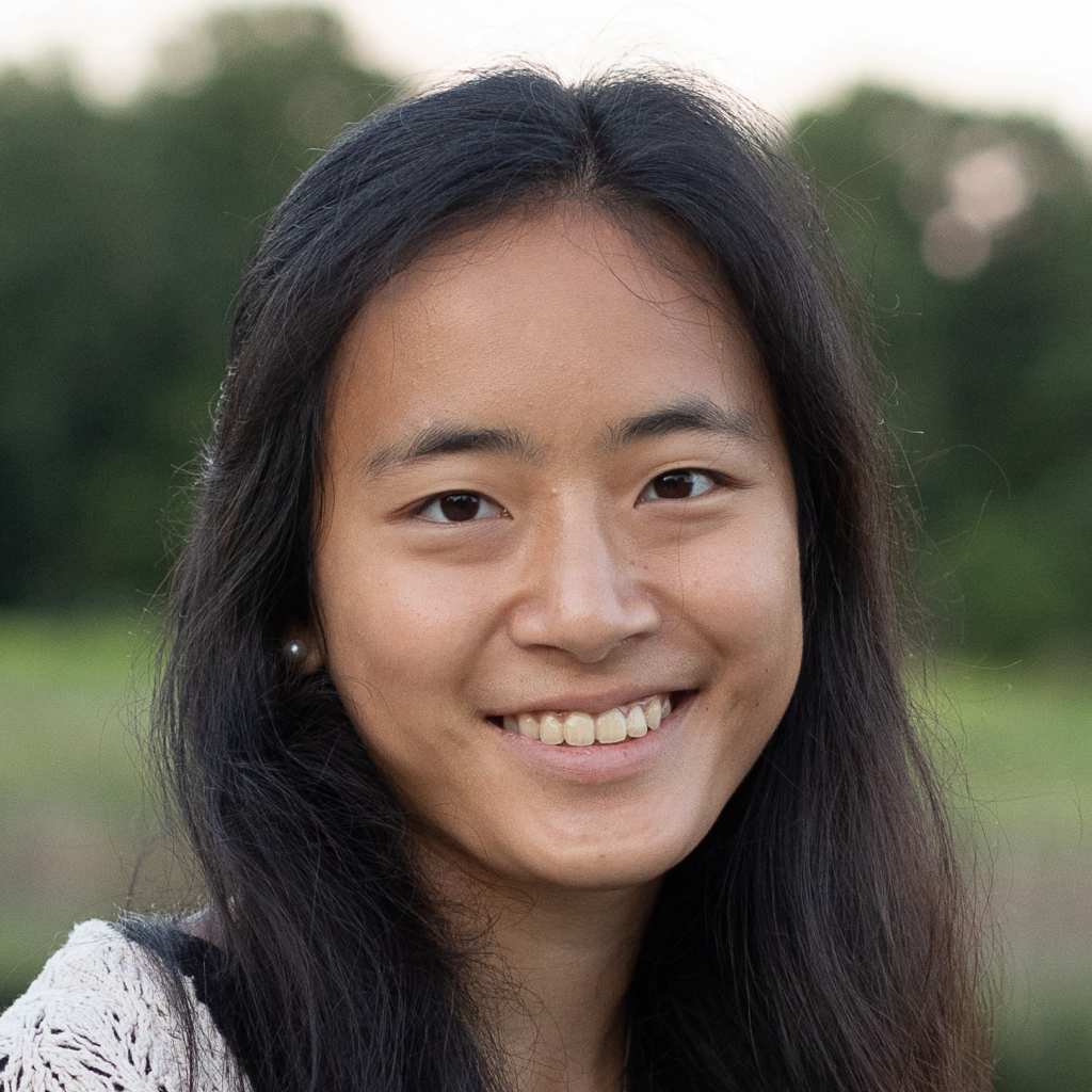 Elanor Tang (headshot) smiles at the camera against a blurred background of grass and trees.
