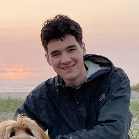 William Wang smiles at the camera, kneeling with a small, brown dog. He is wearing a dark windbreaker, and there is a sunset behind him.