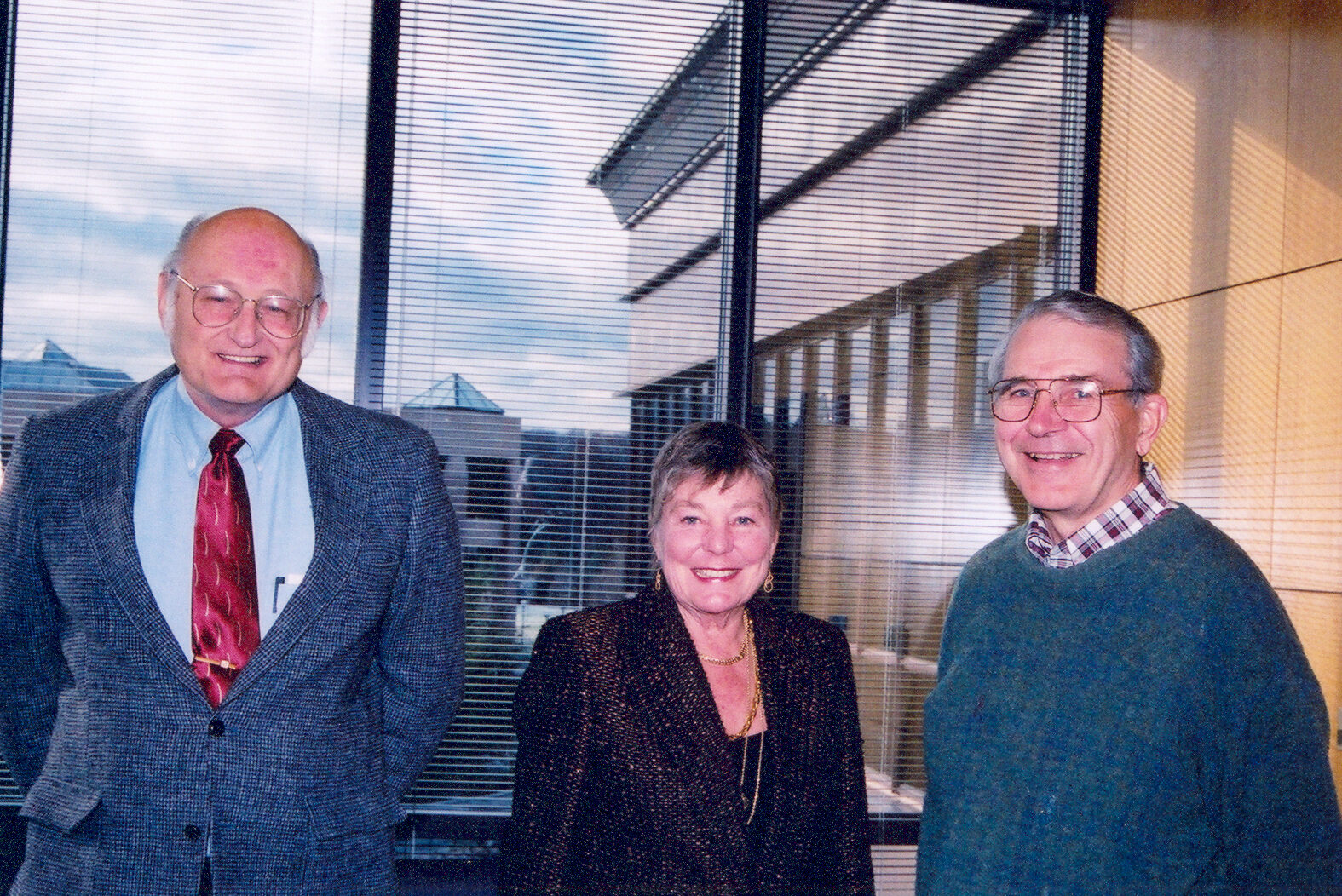 Two men and a woman smile in front of a window in a conference room.