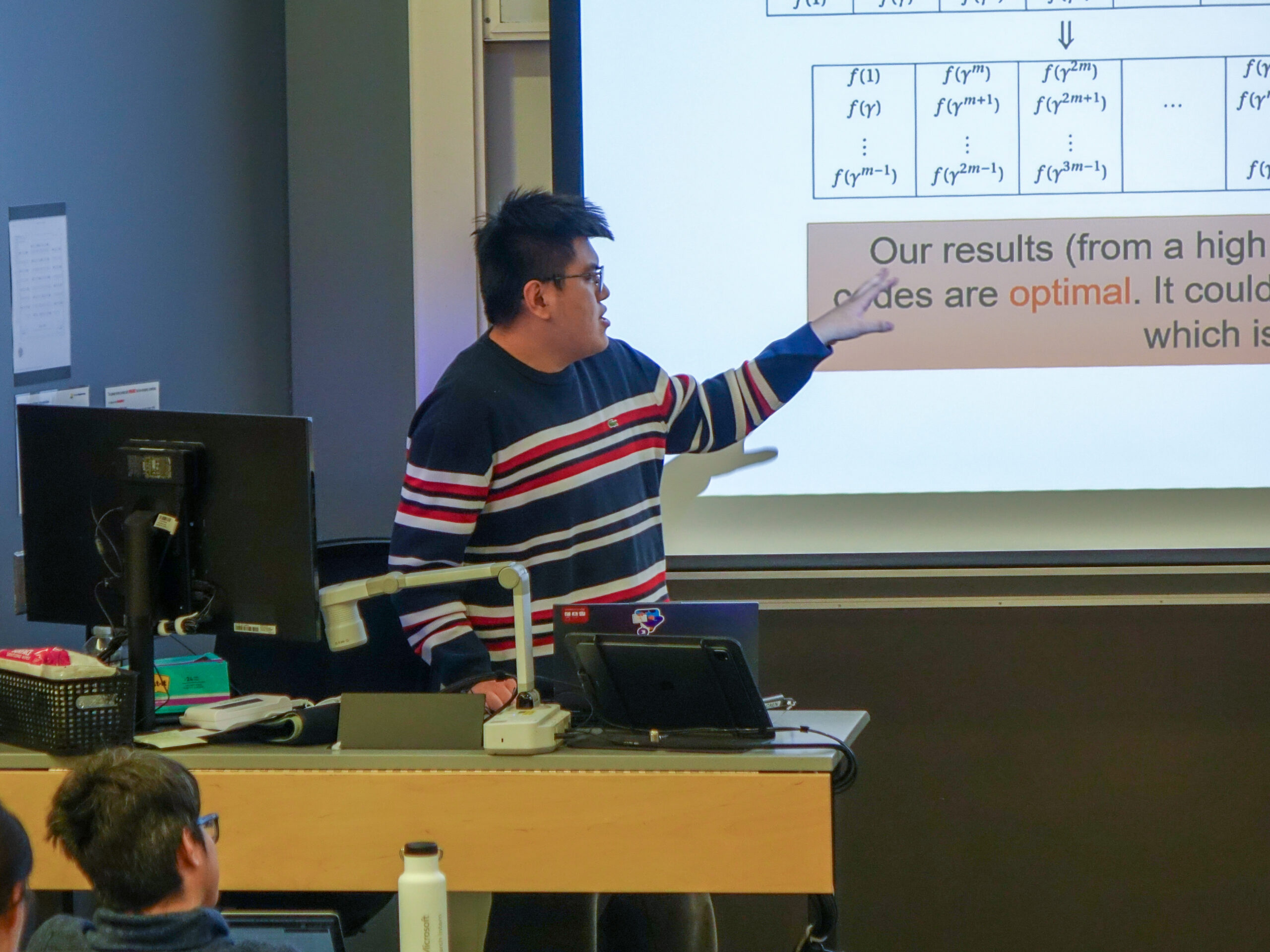 Yeyuan Chen stands presenting at a lectern, he is pointing to a formula on a projector screen