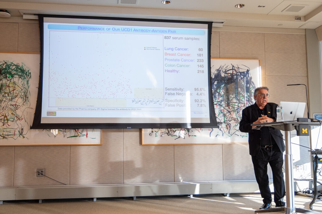 A man stands at a podium and presents a slide titled, "Performance of our UCD1 antibody-antigen pair" with a scatter plot on it.