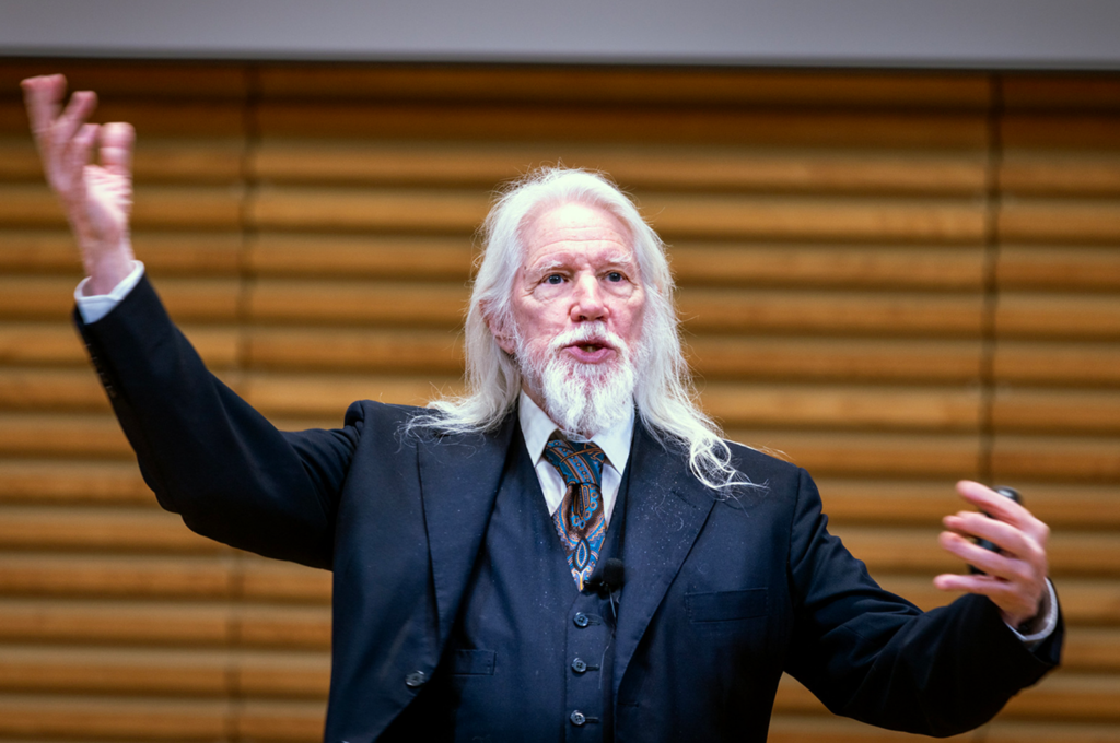 A close-up view of Whitfield Diffie delivering a lecture with his arms held aloft in an animated gesture.