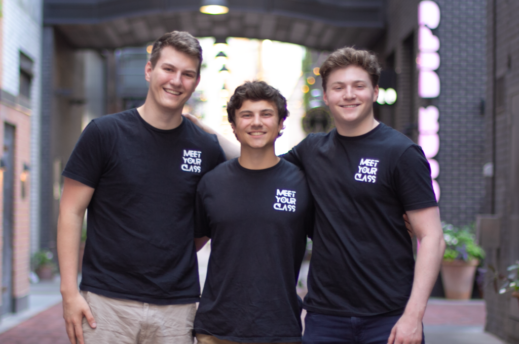 Blake Mischley, Kaleb Schmottlach, and Jonah Liss stand side by side, smiling, in front of a sunny alleyway