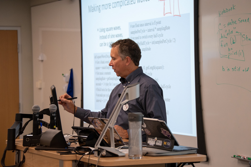 Mark Guzdial writes on a digital screen at the front of a classroom while delivering a lecture