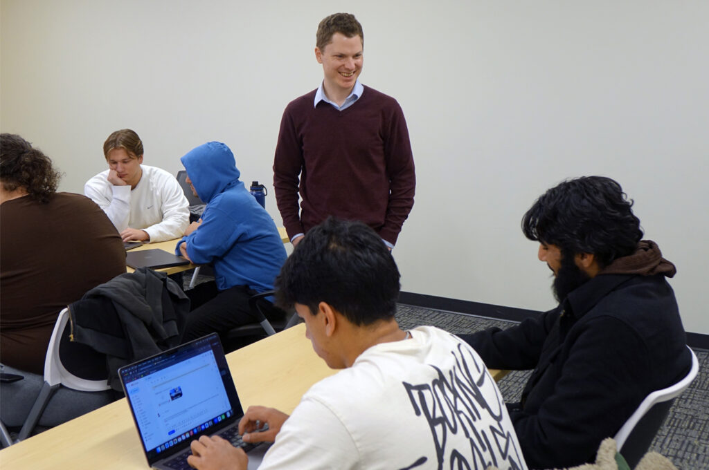 An instructor chatting with seated students in the classroom.