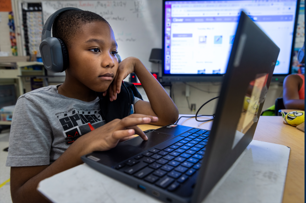 A student wearing headphones concentrates on the digital coursework displayed on the screen of their laptop.