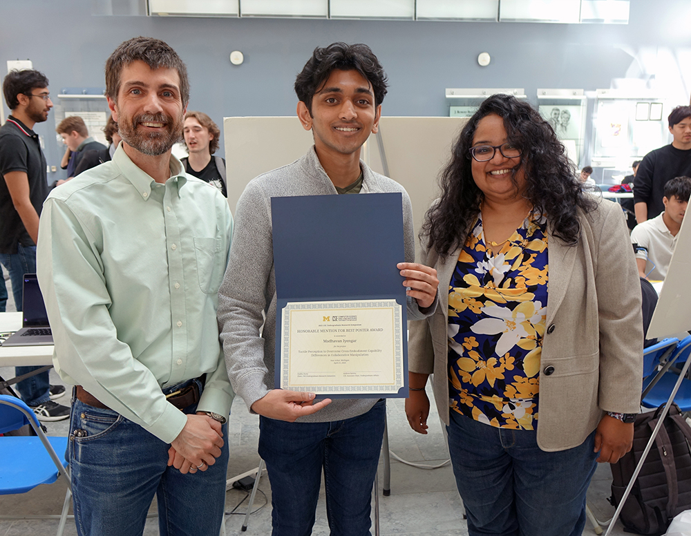 Photo of student holding award certificate, flanked by two faculty members
