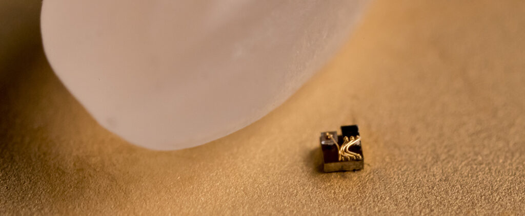 a square device with 4 wires on top of it next to a grain of rice