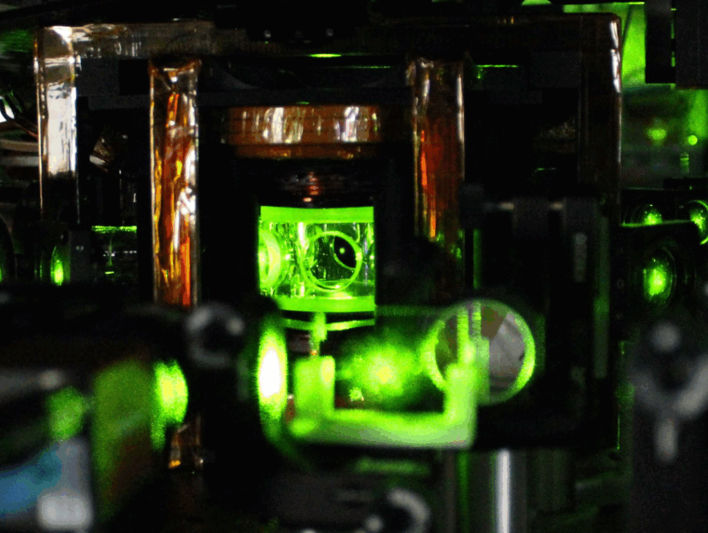 Circular glass windows in a piece of machinery illuminate green with laser light.