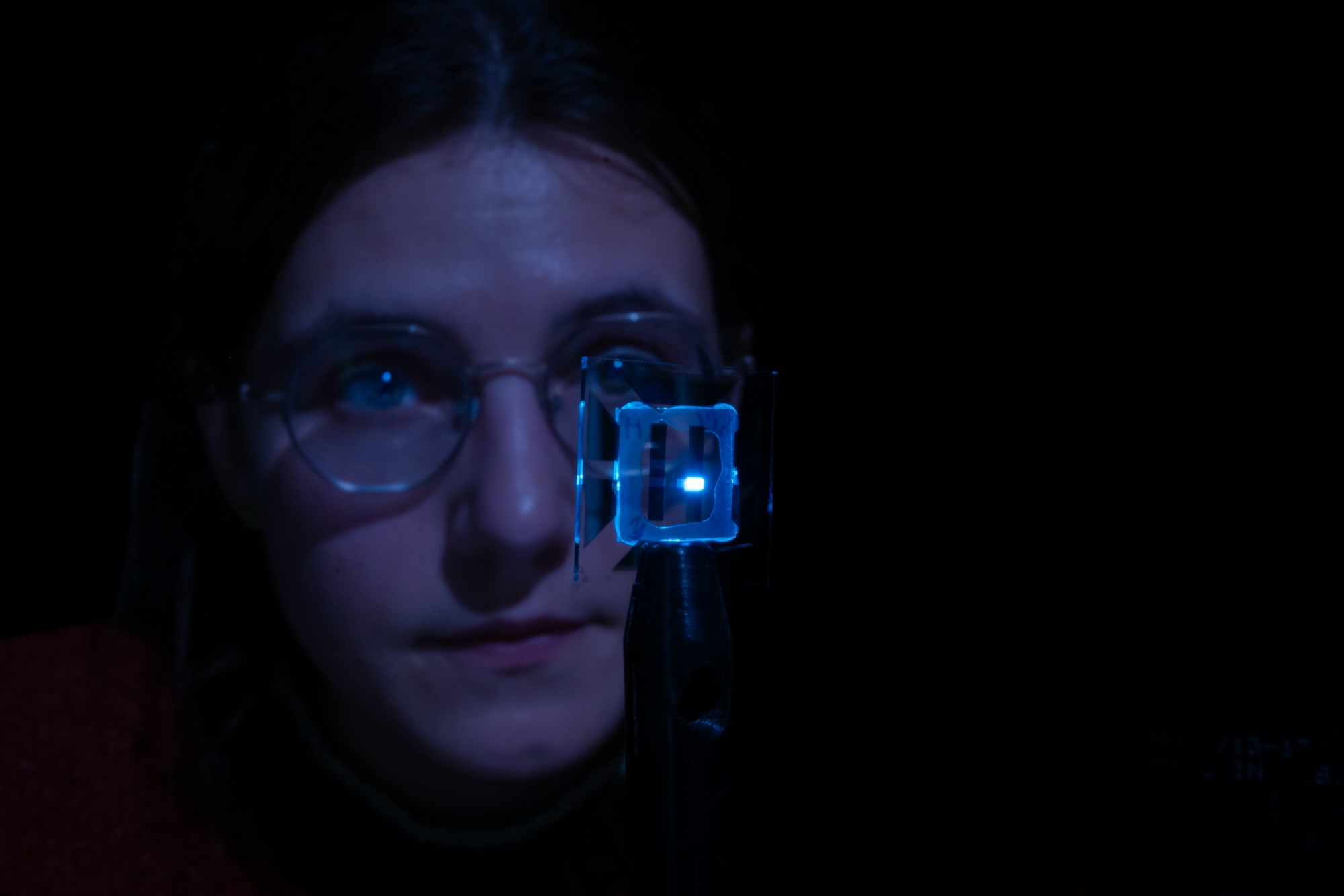 Claire Arneson holds the transparent square with the glowing blue rectangle, her face illuminated by its light.