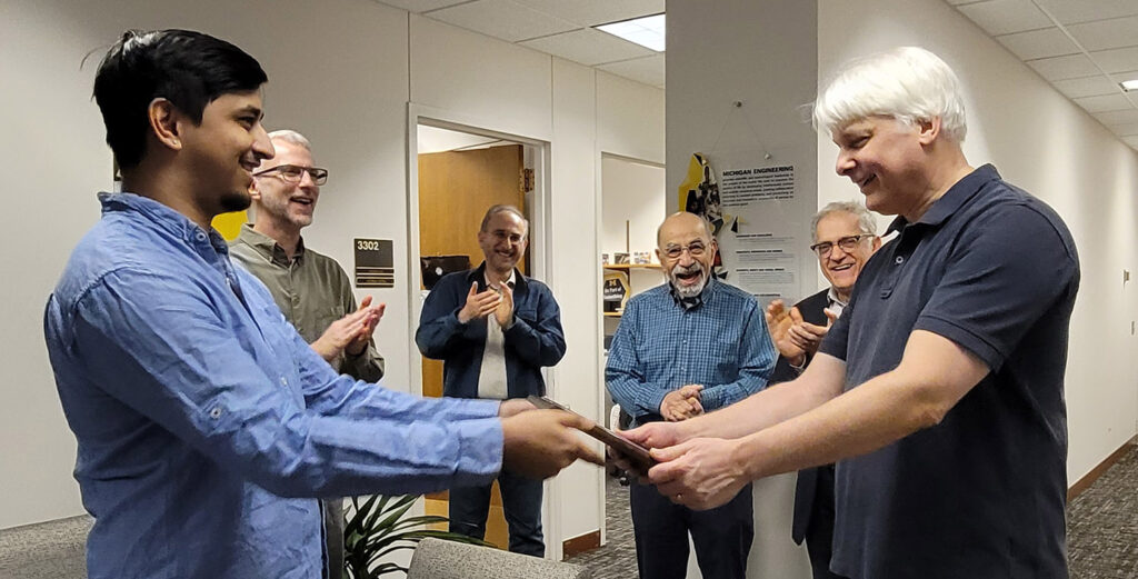 A student hands the plaque to Leland Pierce, while colleagues clap in the background