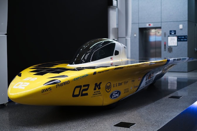 Millennium is parked in the atrium of a building with a gray, linoleum floor. Its sleek, yellow body gleams as it reflects the atrium's fluorescent lights..